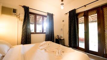 Una habitación de hotel con cama, ventana con cortinas, equipo de aire acondicionado y una lámpara en el techo.