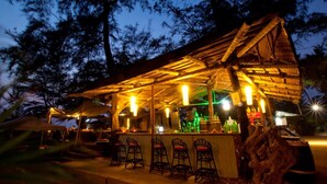 A rustic outdoor bar with wooden beams, a thatched roof, and several bar stools. - Montego Bay Beach Village (Morjim)