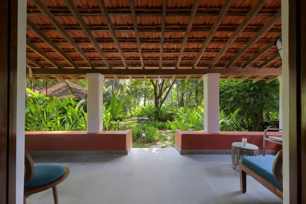 A covered outdoor seating area with a view of a lush garden. - Montego Bay Beach Village (Morjim)