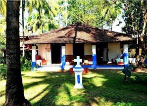 A small, single-story building with a thatched roof, surrounded by lush greenery.