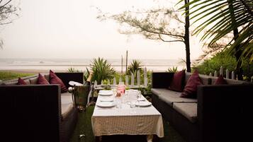Un área de comedor al aire libre con una mesa preparada para cuatro personas, con vista a la playa.