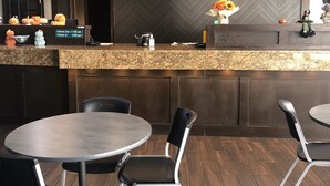 A restaurant interior with a herringbone-patterned wall, a marble counter, and black chairs around round tables.
