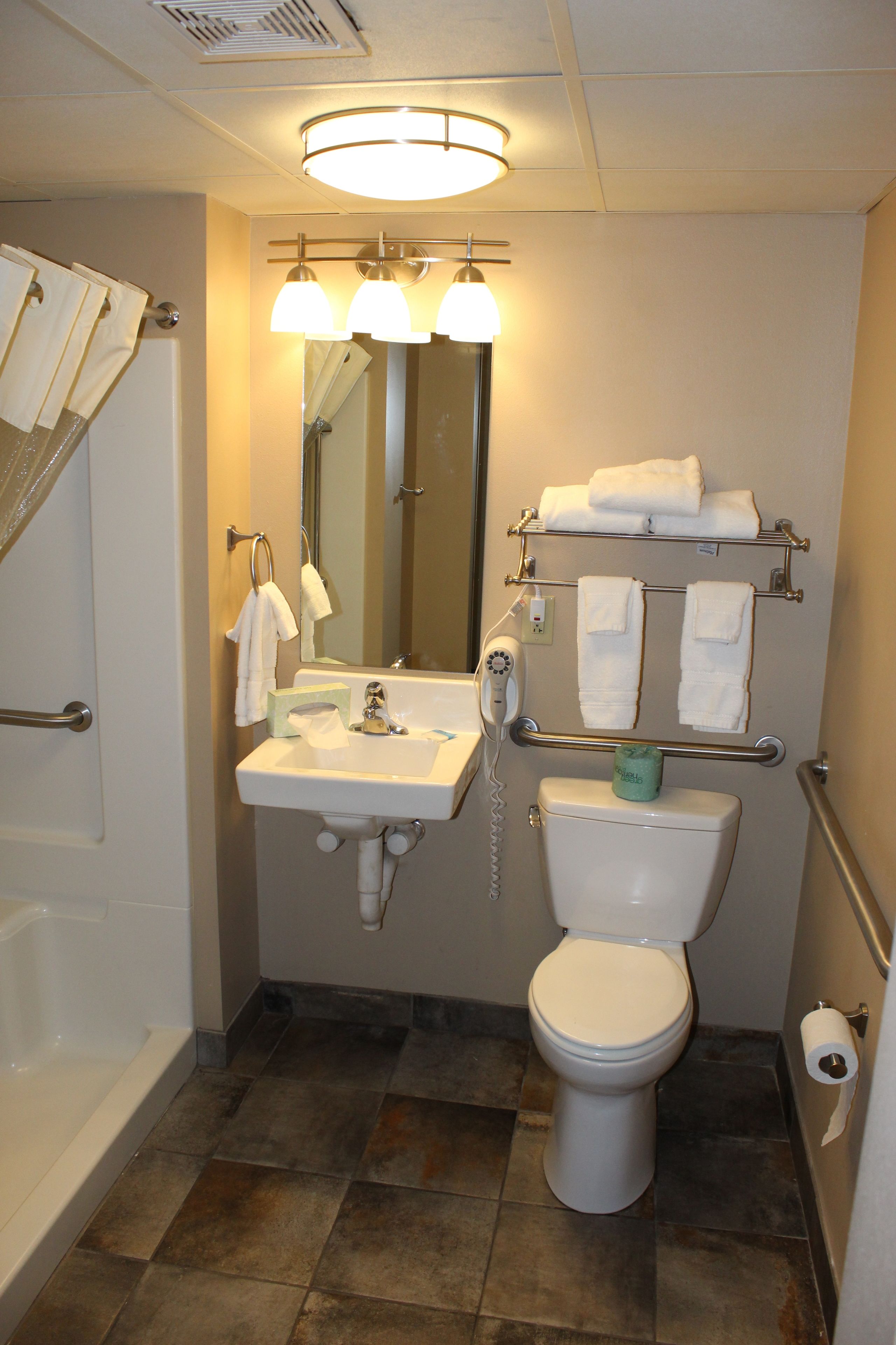 Baño pequeño y funcional con lavamanos, inodoro y espejo compacto. Varias toallas cuelgan de un perchero sobre el inodoro.