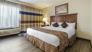 A hotel room with a large bed, a bedside table with a lamp, a window with curtains, and a painting on the wall.