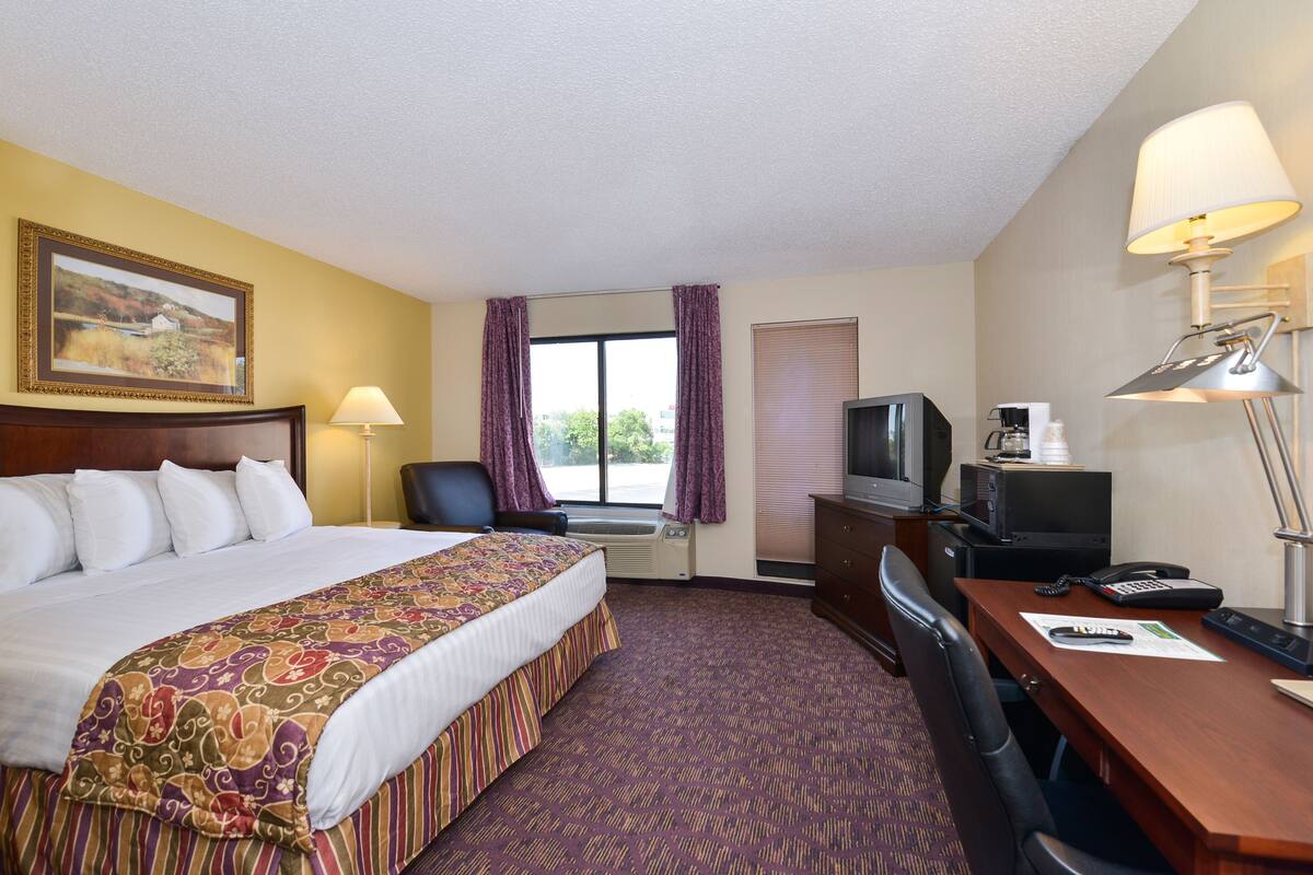A hotel room with a bed, desk, chair, TV, and a window with curtains.