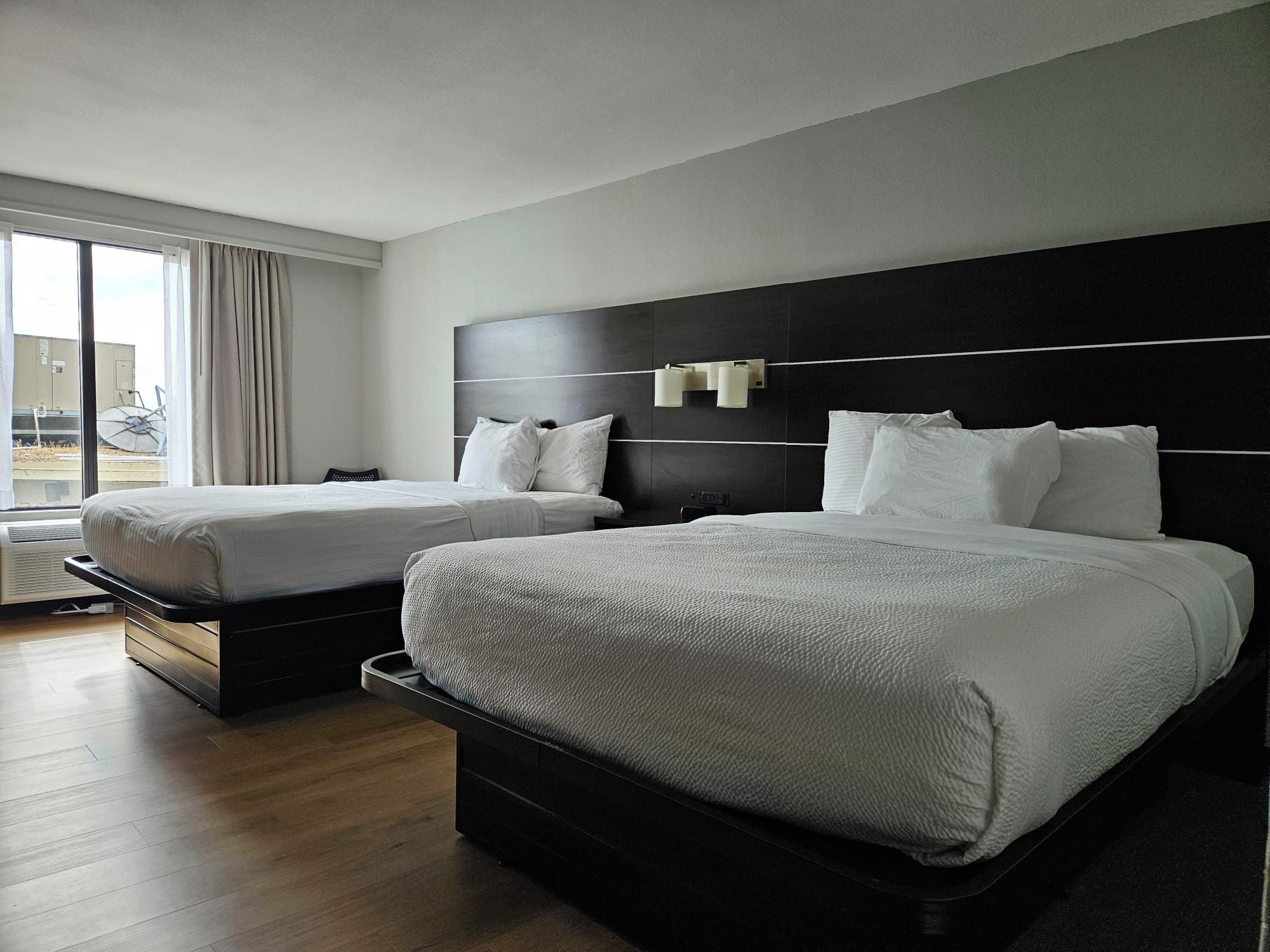 Una habitación de hotel con dos camas, un ventanal con cortinas y vistas al exterior.