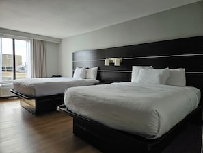 A hotel room with two beds, a large window with curtains, and a view of the outside. - Lamplighter Inn & Suites - South (Springfield)