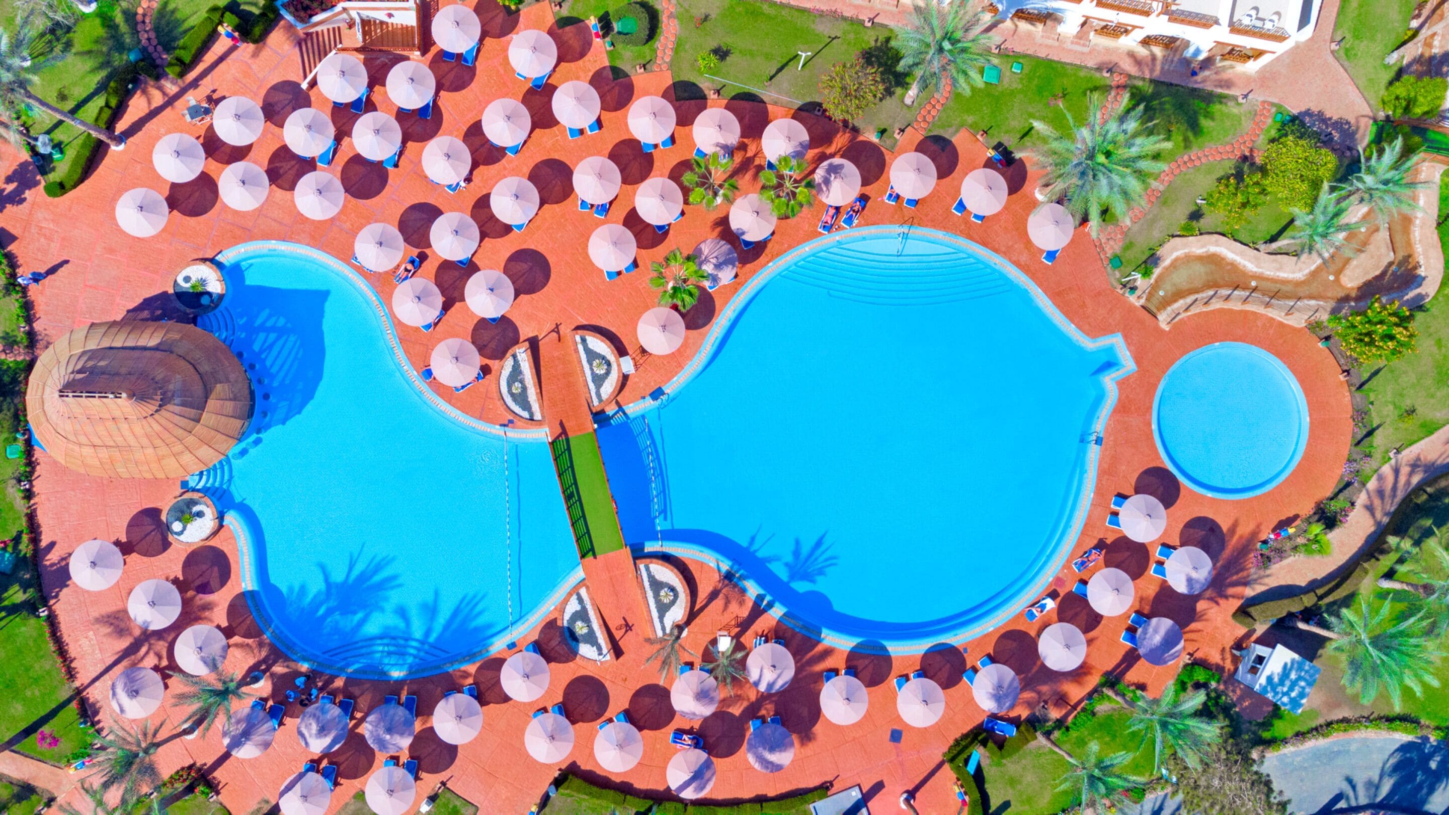 Vue aérienne d’un complexe hôtelier doté de plusieurs piscines, de parasols et de palmiers.