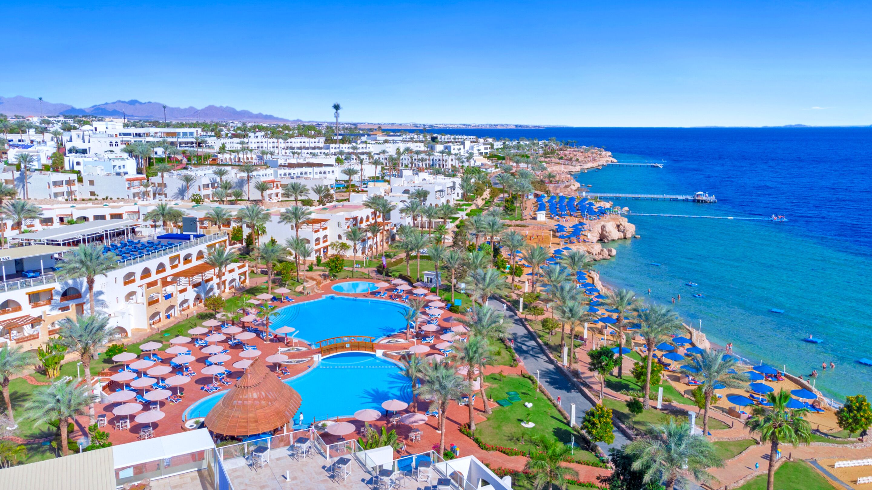 Un resort con varias piscinas, zonas de playa y vista al mar.
