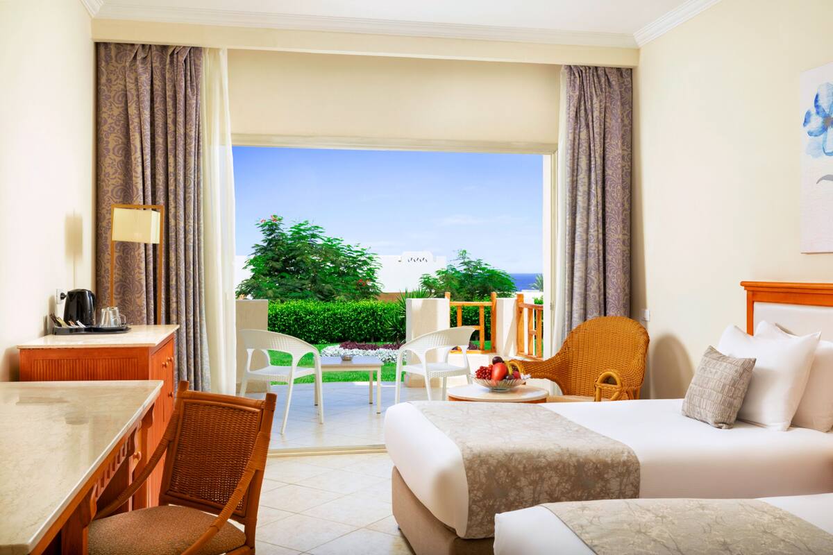 A hotel room with a bed, a desk, chairs, and a view of the outdoors.