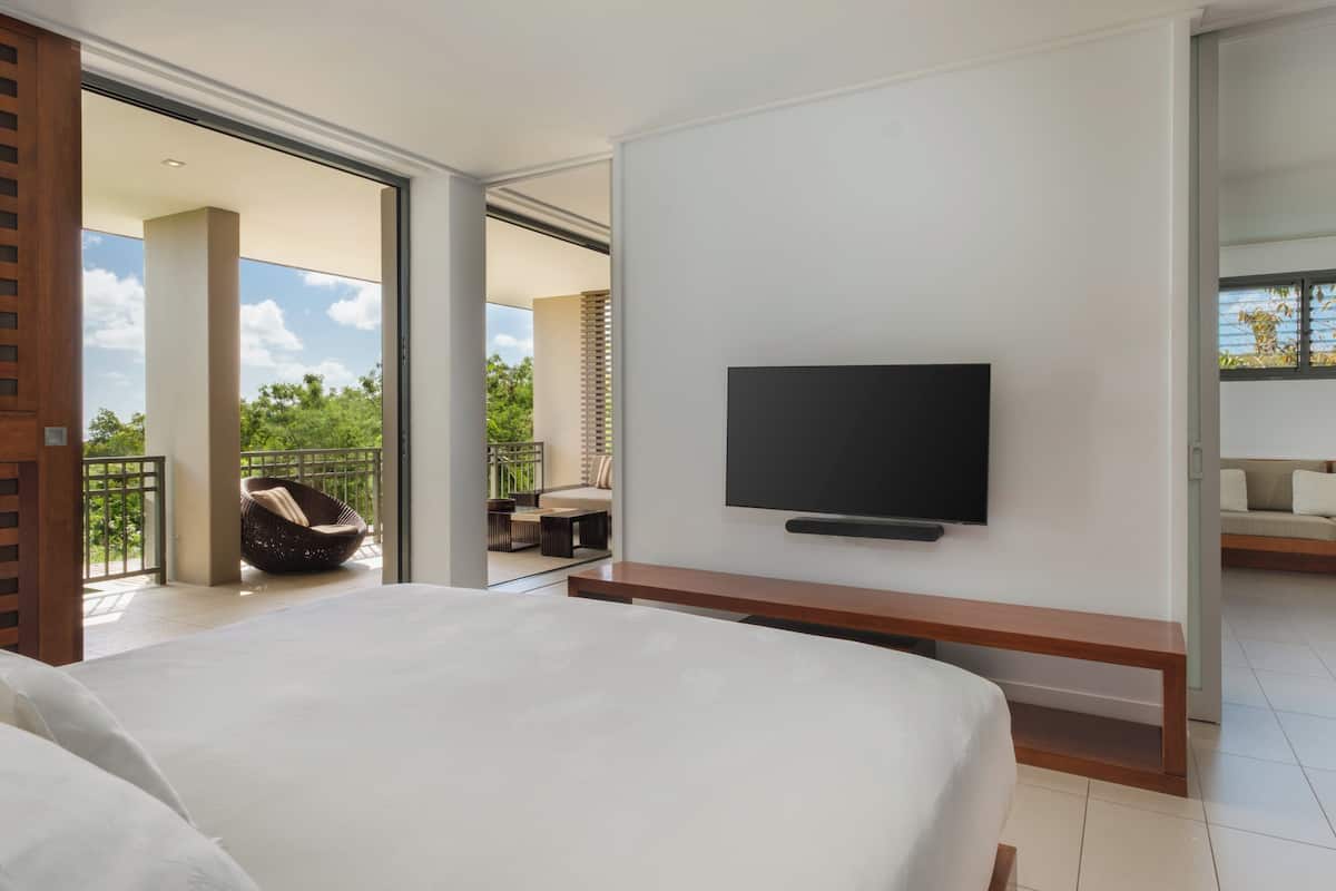 Ein modernes Hotelzimmer mit einem großen Bett, einem flachbildfernseher an der Wand und einem Balkon mit Sitzgelegenheit.