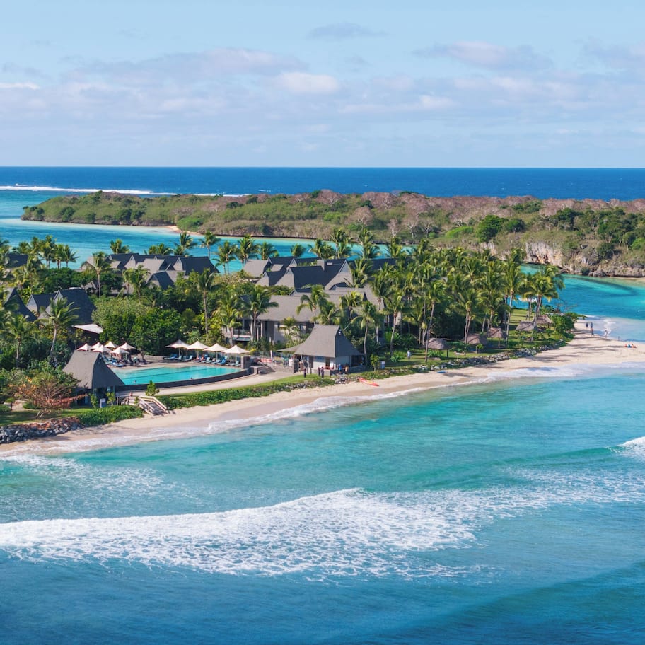 A resort with multiple bungalow-style buildings, a beach, and clear turquoise waters.
