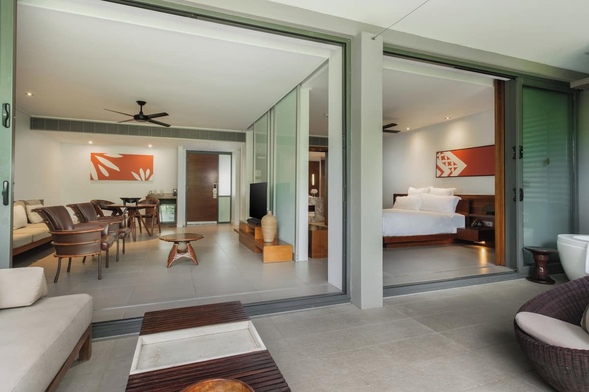 Ein modernes Hotelzimmer mit einer Couch, Sesseln, einem Couchtisch, einem Fernseher und einem Bett.