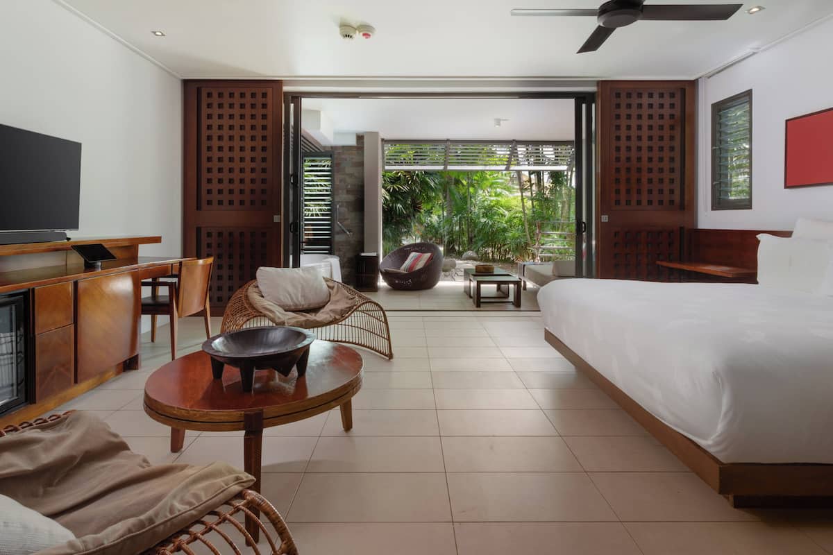 Ein modernes Hotelzimmer mit Bett, Fernseher, Esstisch und Balkon mit Pflanzen.