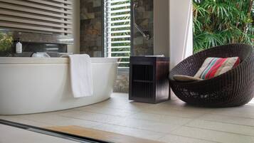 Un baño con bañera, una silla de mimbre con cojín y una ventana con persianas.