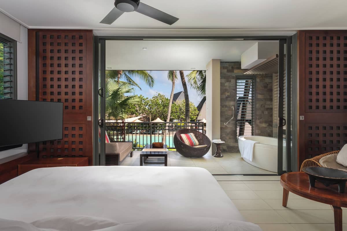 Ein Hotelzimmer mit einem großen Bett, einem Fernseher, einem Balkon mit Pool und einem Wellnessbereich.