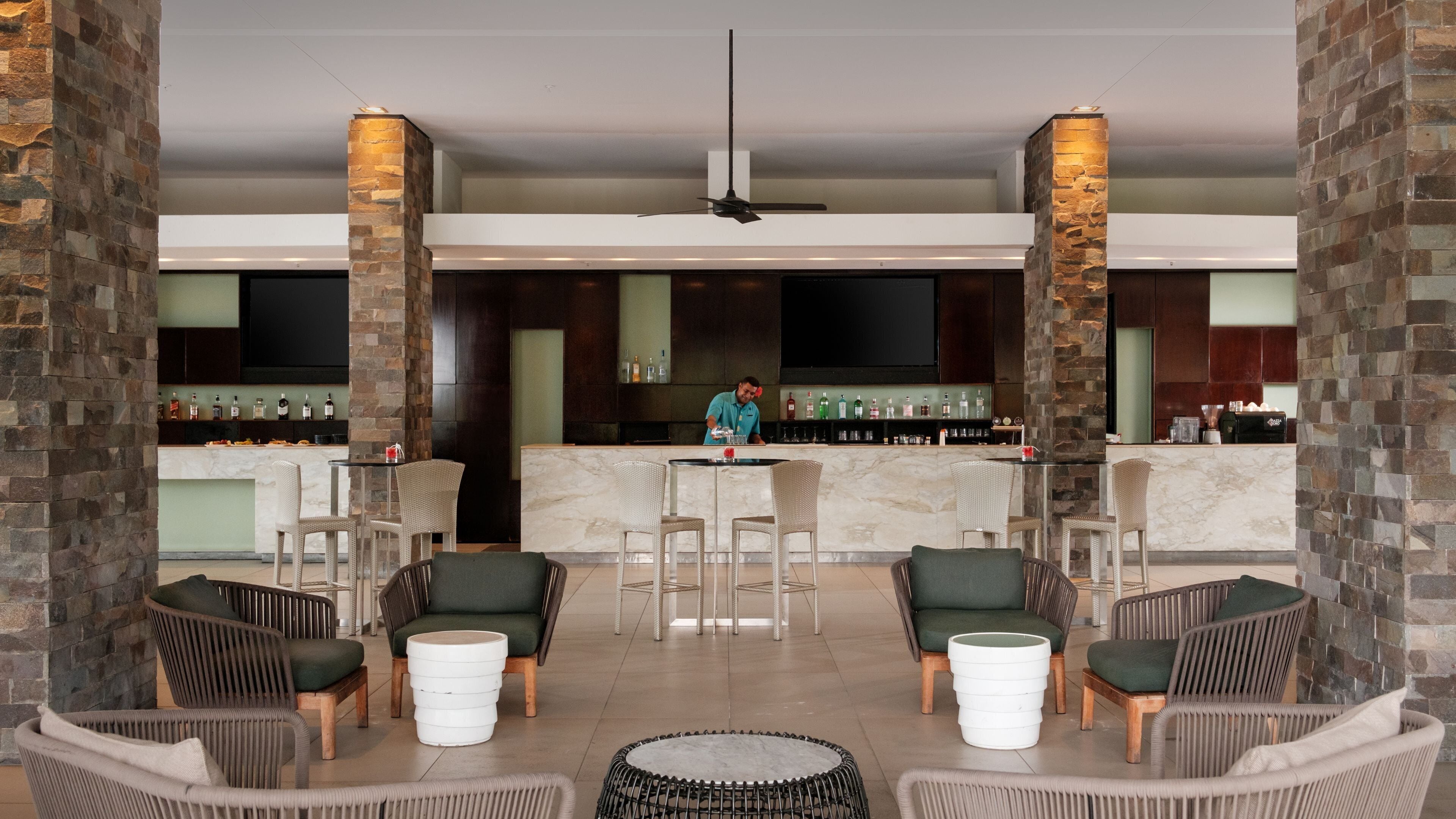 A lobby with wicker chairs, a bar area, and stone pillars.