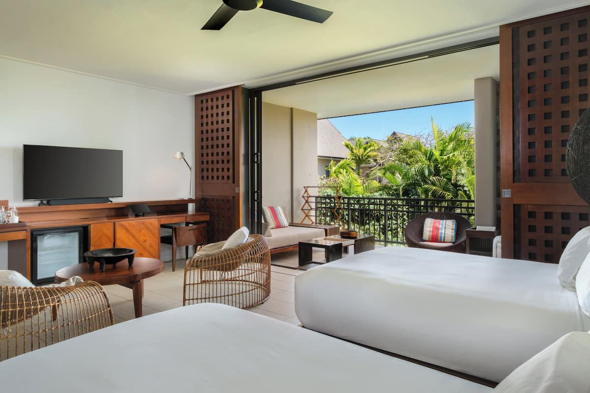 Ein Hotelzimmer mit Balkon, Fernseher, Schreibtisch und zwei Betten.