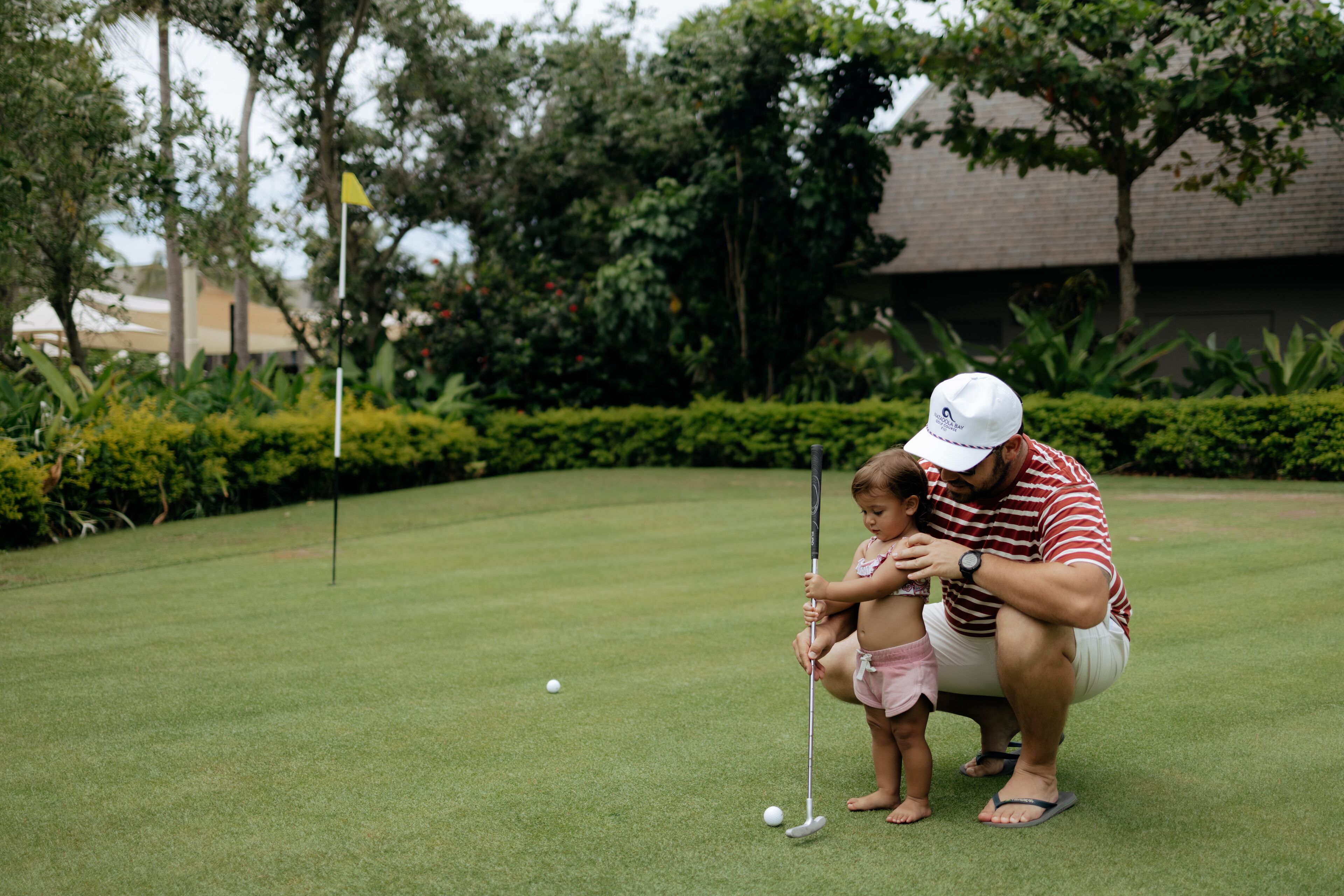 Un campo de golf con un putting green, árboles y un edificio al fondo.