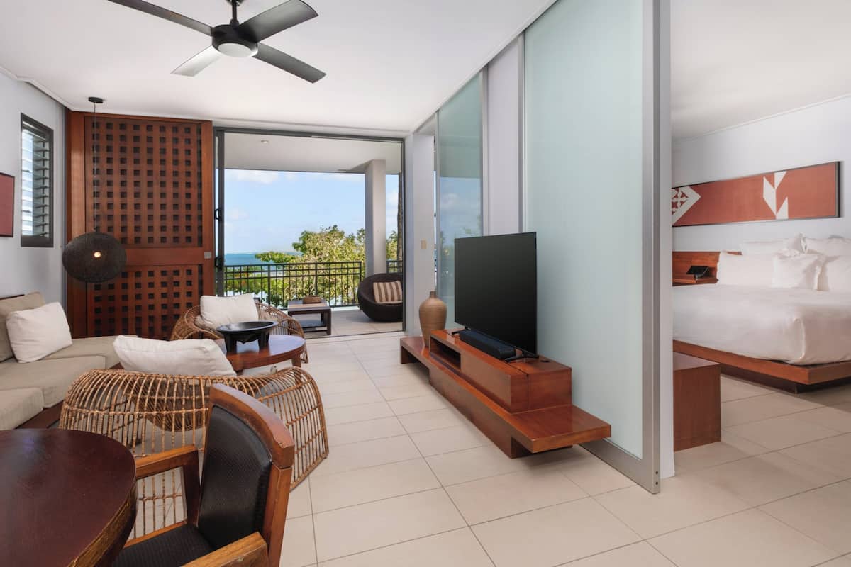 Ein modernes Hotelzimmer mit Balkon, Flachbildfernseher, Sofa, Esstisch und Bett.