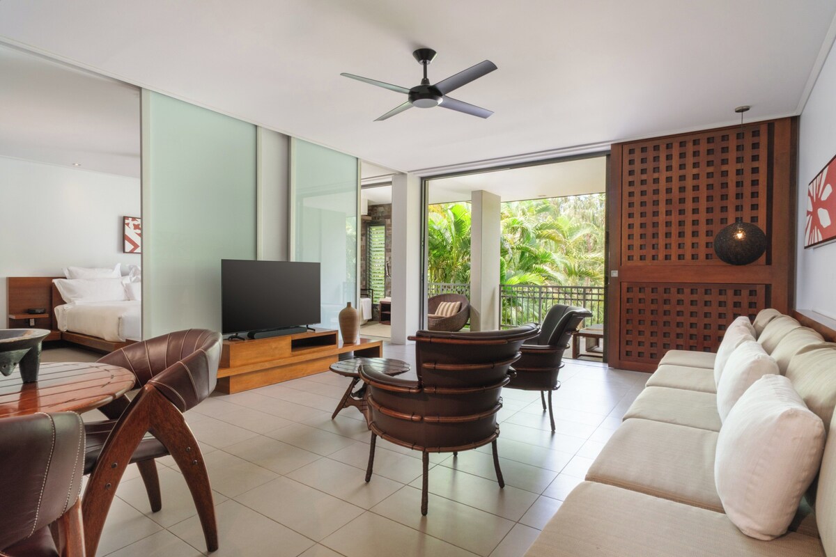 A modern living room with a sofa, chairs, a TV, and a dining area.