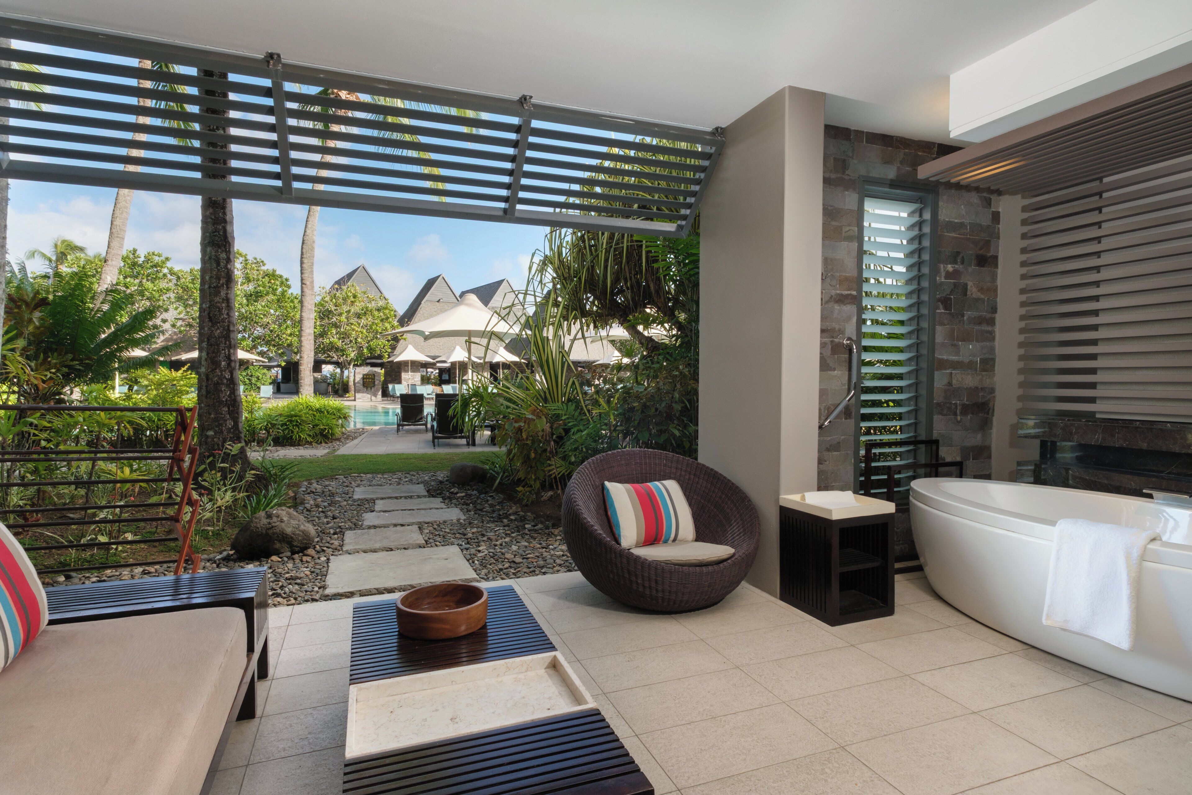 Un espacio exterior moderno con una sala, un sillón, un cuenco de madera y una bañera.