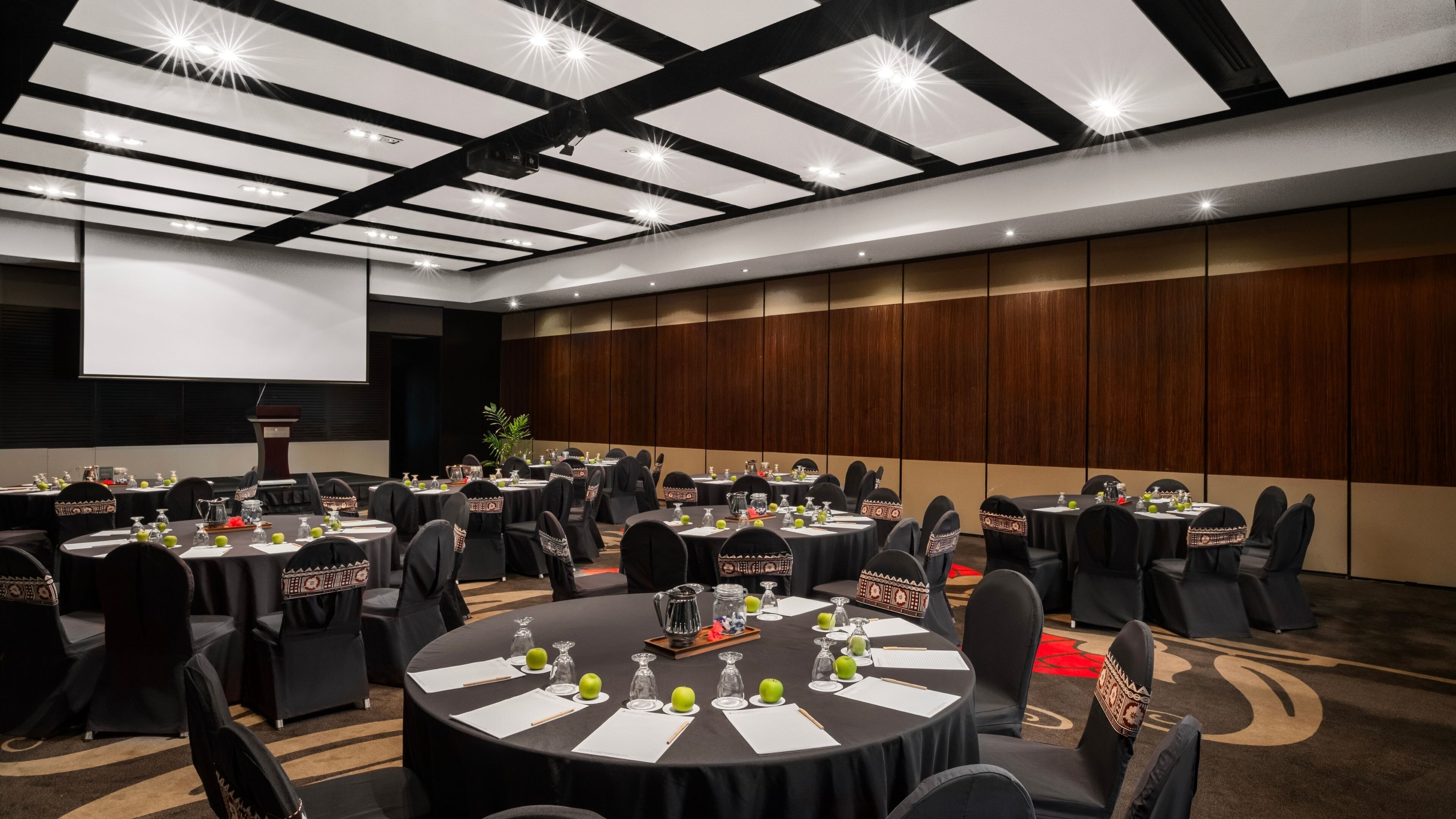A conference room with round tables, black chairs, and a projector screen.