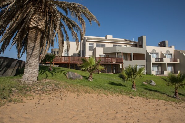 A modern hotel with multiple balconies, palm trees, and a sandy landscape.