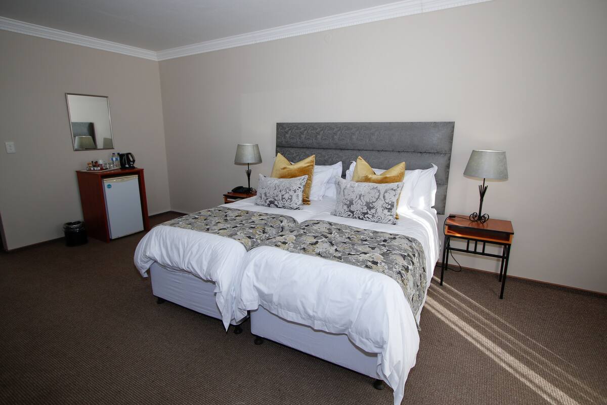 A hotel room with a large bed, two bedside tables, a desk, a mirror, and a small refrigerator.