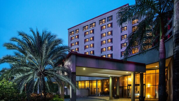Un hotel de varios pisos con un vestíbulo cubierto y palmeras al frente.