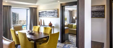 A hotel room with a dining area featuring a table and chairs, a sofa, and a large window with curtains.