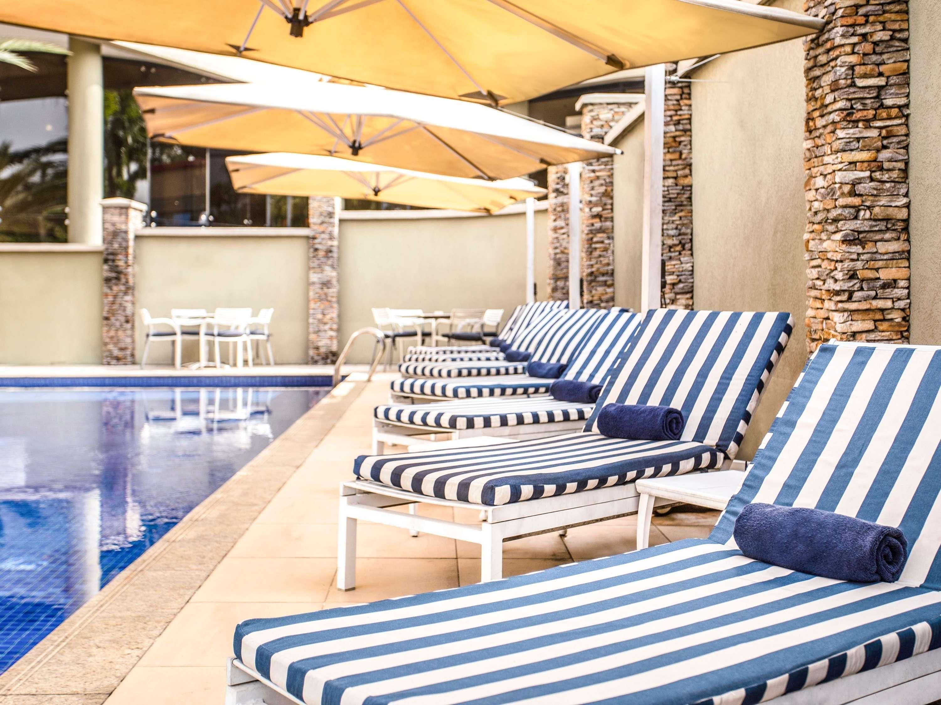 Un área junto a la piscina con sillones de descanso y sombrillas.
