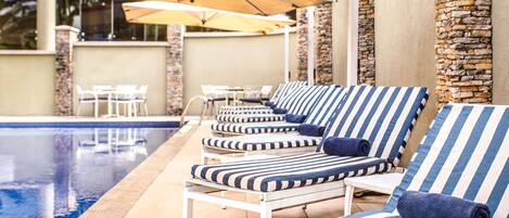 Un área junto a la piscina con sillones de descanso y sombrillas.
