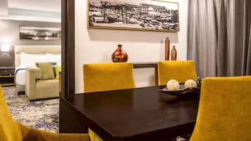 Hotelkamer met een eettafel, gele stoelen, een bank, een bed en een lijst met een stadsgezicht aan de muur.