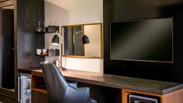 A modern room with a dark wood desk, a black leather chair, a small refrigerator, a microwave, and a large mirror.