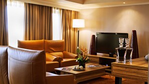 A hotel room with a leather sofa, a flat-screen TV, a wooden coffee table, and a lamp.