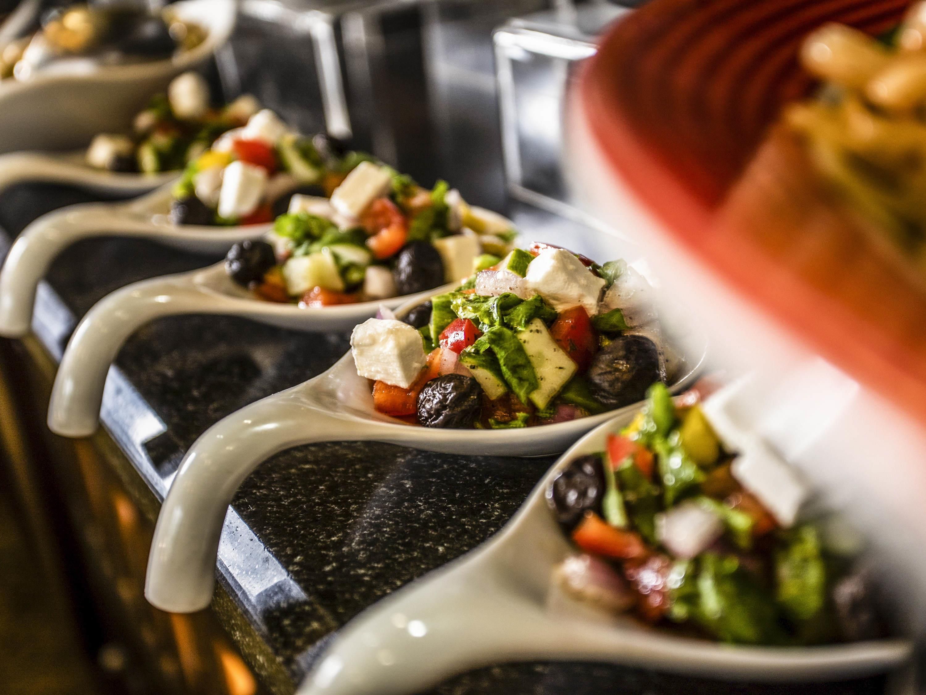 A series of white spoons filled with a salad, placed on a dark countertop.