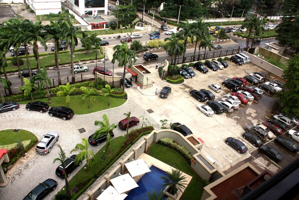 Un estacionamiento con varios coches, un área pequeña de piscina y palmeras.
