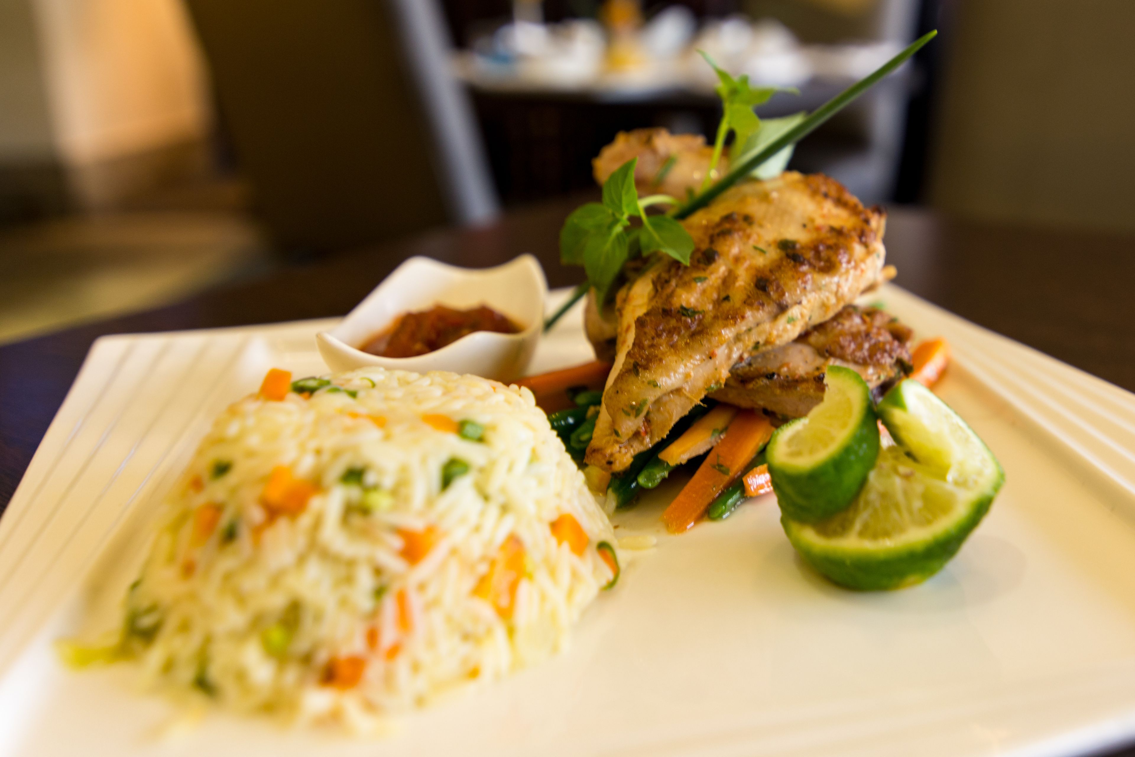 A plate of food with rice, vegetables, and a piece of meat, possibly chicken, garnished with herbs.