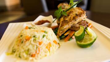 A plate of food with rice, vegetables, and a piece of meat, possibly chicken, garnished with herbs.