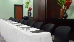 Un salón de conferencias con una larga mesa, sillas y jarrones con flores.