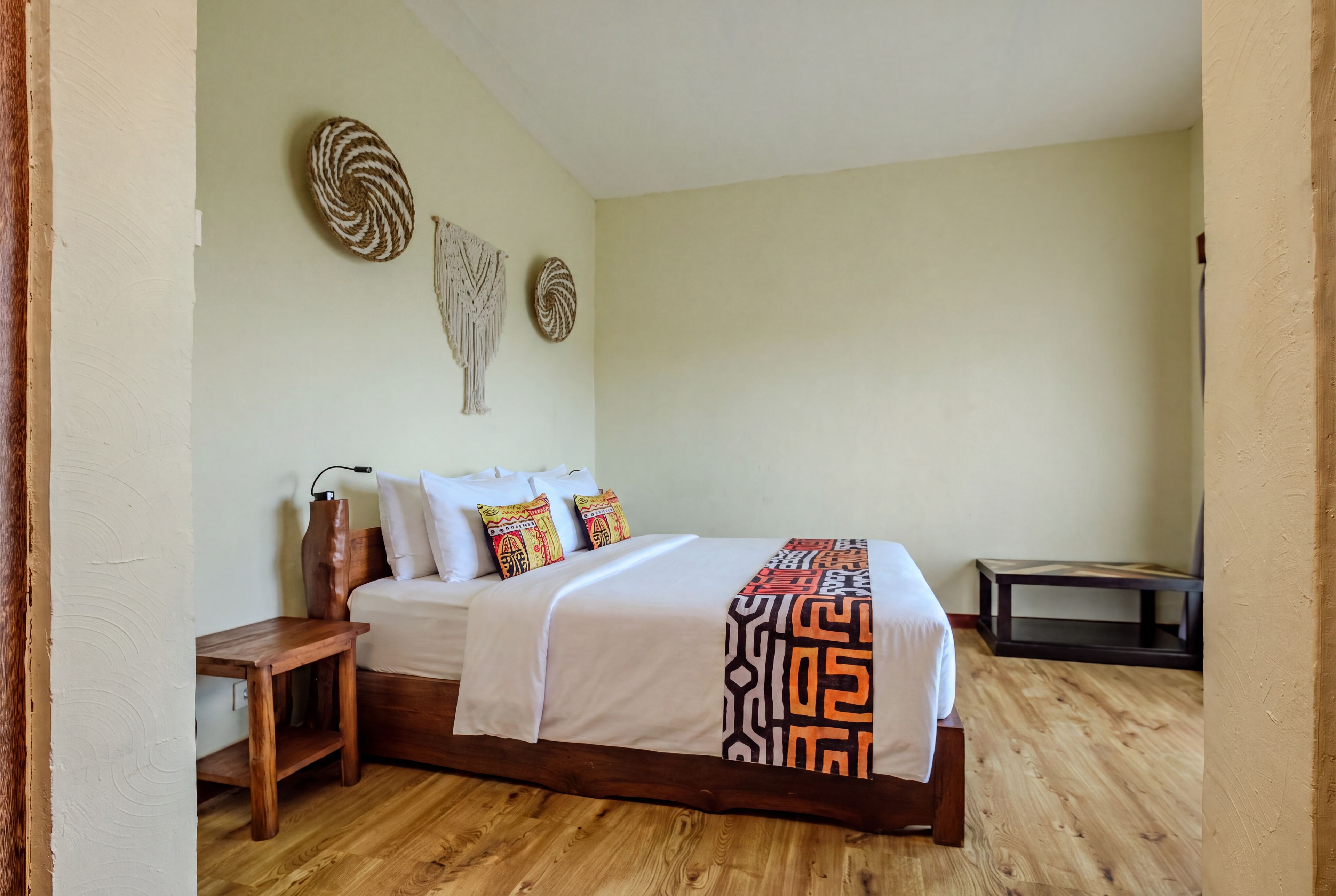 A bedroom with a wooden bed, white bedding, and two decorative wall hangings.