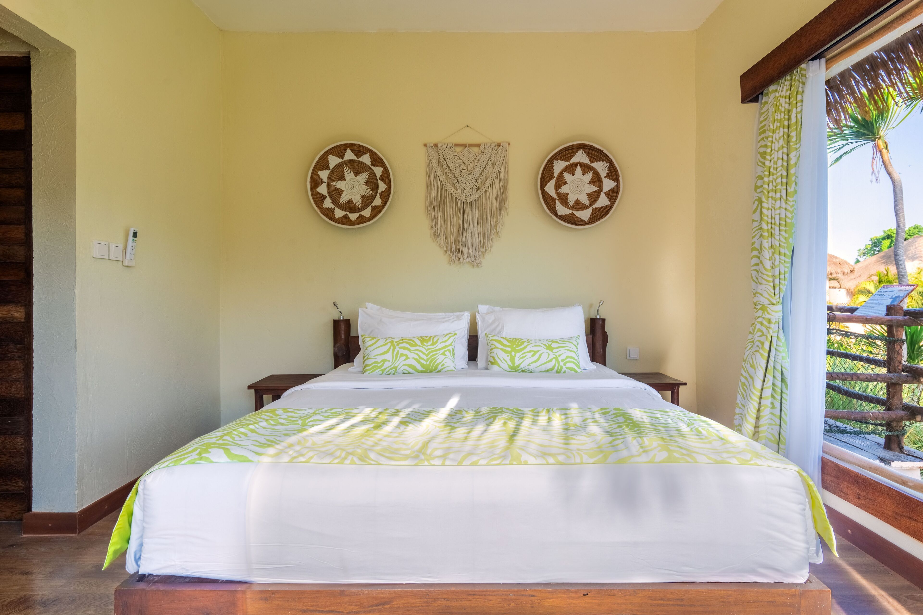 Una cama con una colcha verde y blanca estampada, dos mesitas de noche, y una pared con dos adornos circulares y un adorno de macramé.