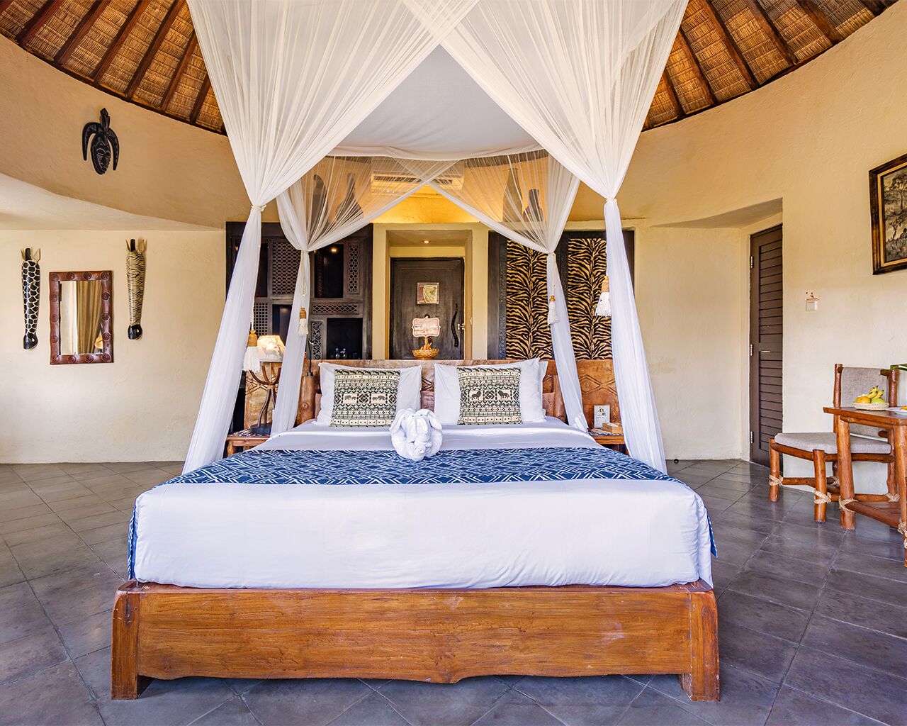 A large bed with a canopy, a wooden nightstand, a chair, and a table with a fruit bowl.