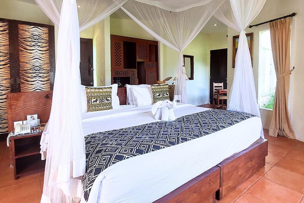 A four-poster bed with white canopy, a wooden headboard, and patterned pillows.