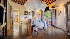 A room with a bed, a nightstand, a lamp, a chair, a TV, and a window with curtains. - Mara River Safari Lodge (Gianyar)