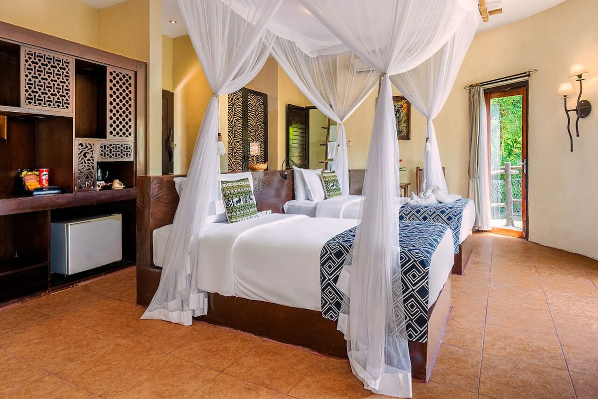 A bedroom with a four-poster bed, a desk with a computer, and a view of greenery outside.