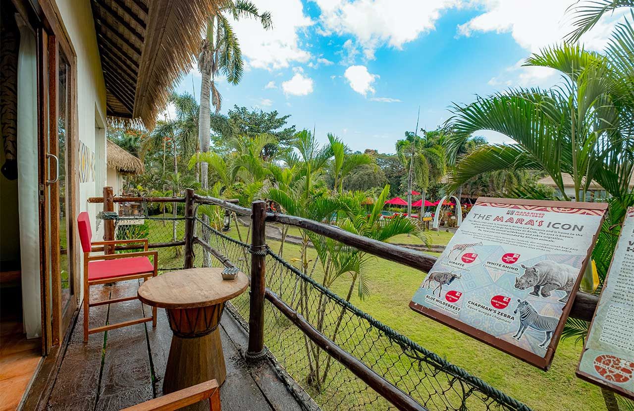 Un balcón con mesa y sillas de madera, un cartel con iconos de animales y vistas a un jardín tropical.