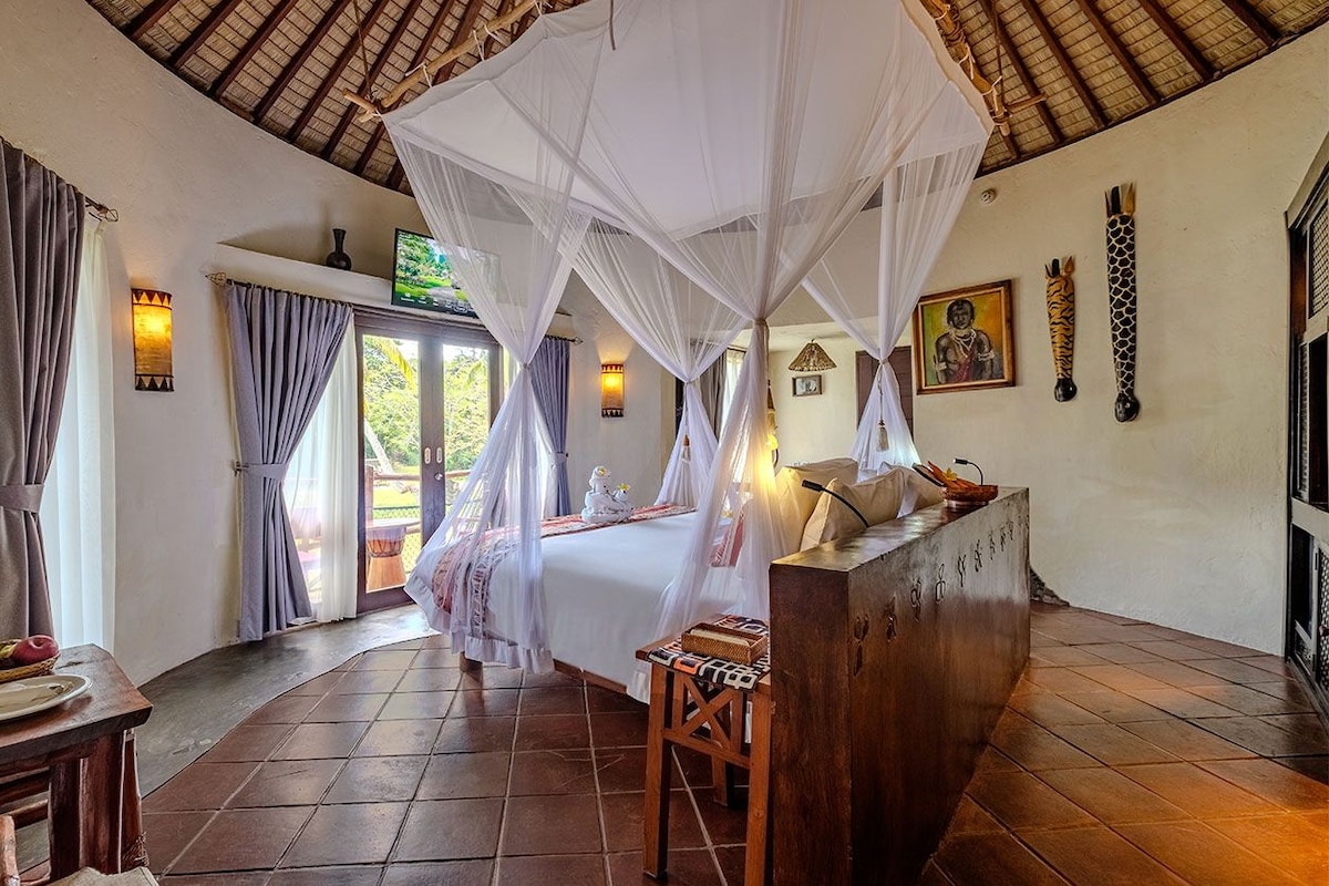 A room with a bed under a canopy, a desk with a chair, and a wall-mounted TV.