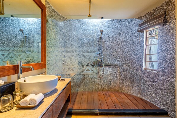 Une salle de bain dotée d’un grand lavabo, d’un meuble-lavabo en bois et d’une douche avec un mur en mosaïque.
